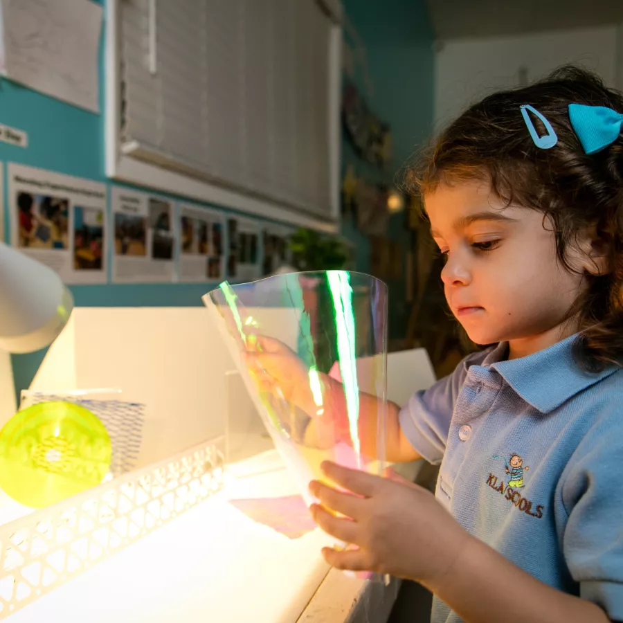 a preschool girl playing with materials on light table in our preschool for 3 year olds