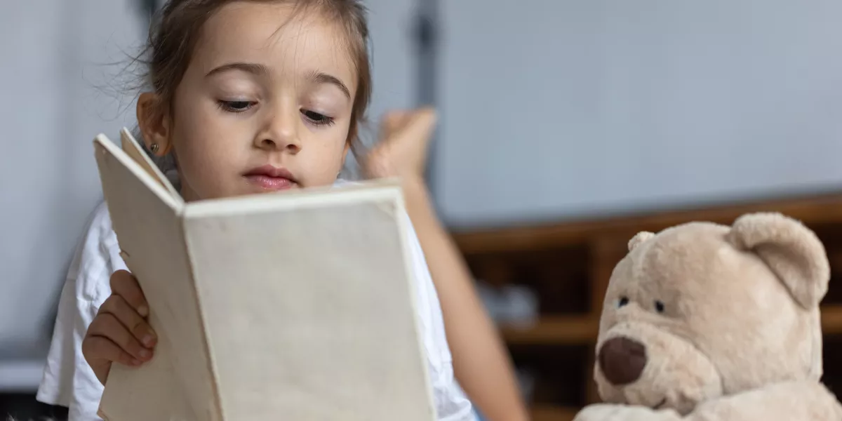 Cute little girl home lying floor with her favorite toy reads book