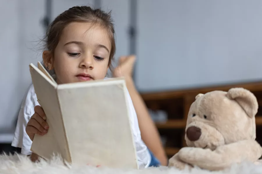 Cute little girl home lying floor with her favorite toy reads book