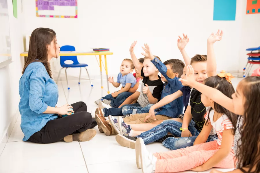 Profile view group preschool students raising their hands trying participate school