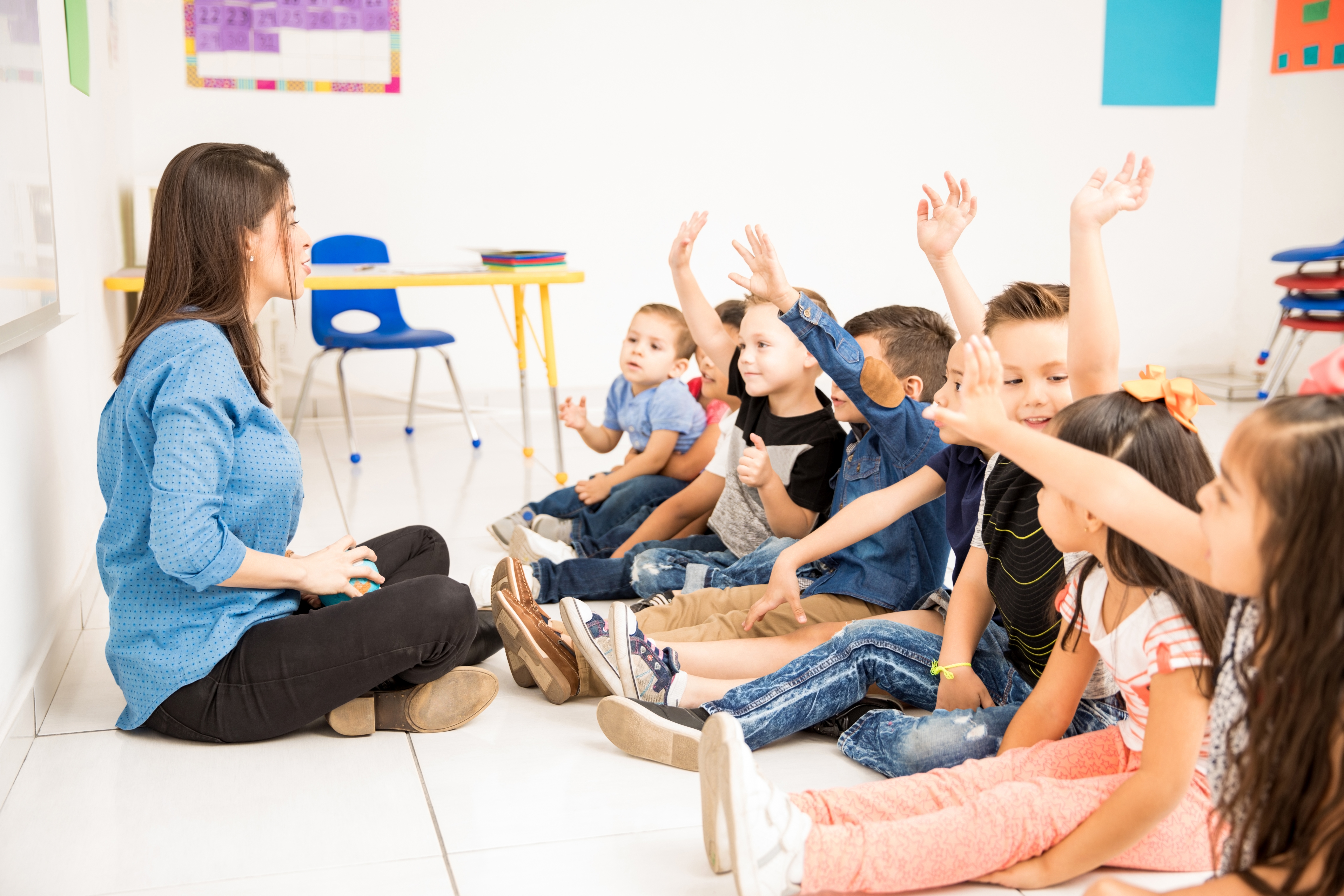 Profile view group preschool students raising their hands trying participate school