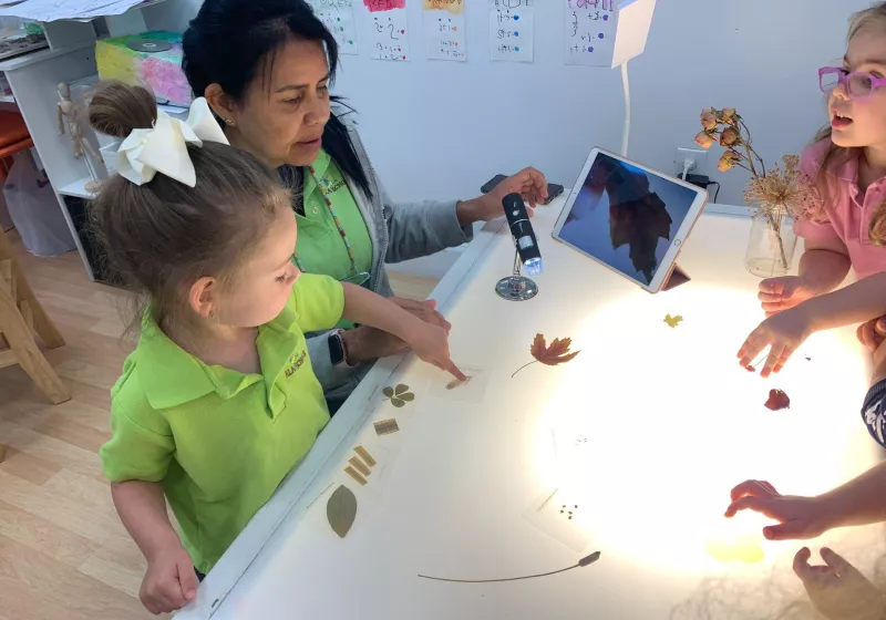 Girls and teacher in light table with Ipad and plants