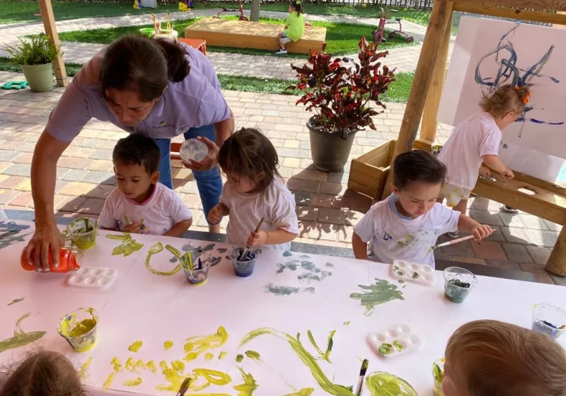 Toddlers painting outside and teacher